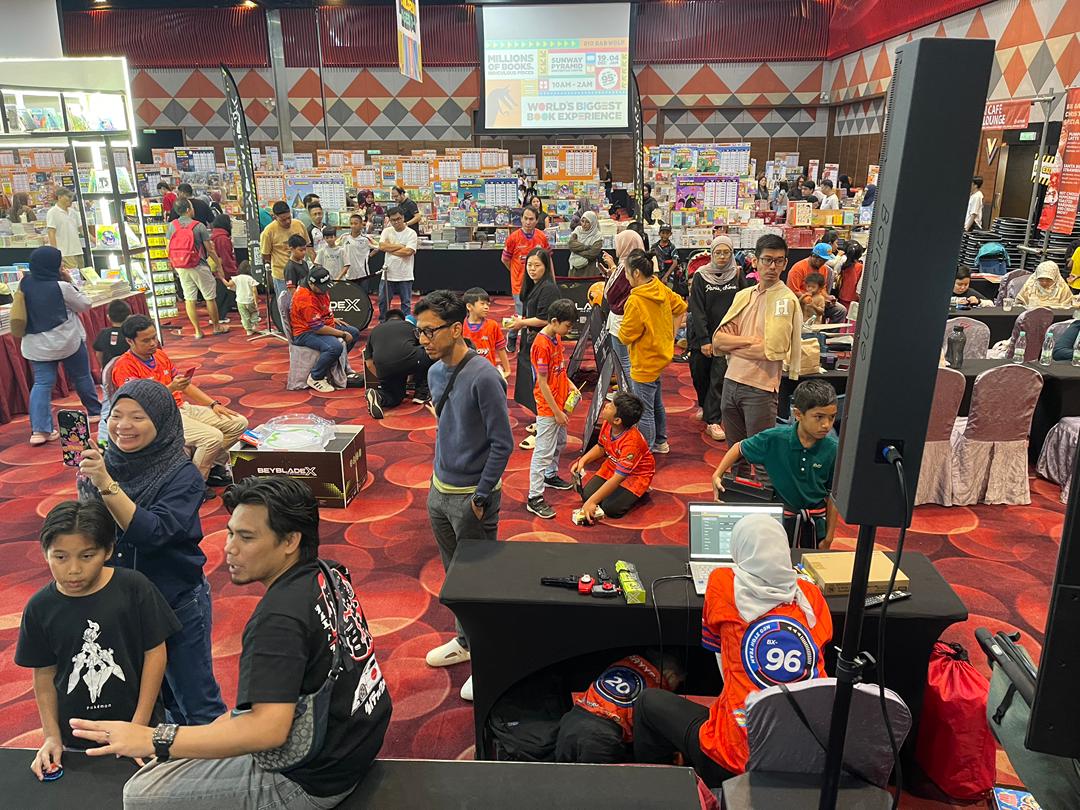 Players and families gathering around Beyblade tournament stations at a book fair